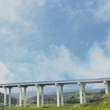 Long, solid bridge spanning across green nature under a blue sky