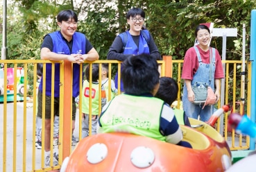 효성나눔봉사단원들이 놀이공원에서 아이들이 즐겁게 놀이기구를 타는 모습을 보며 흐뭇하게 웃고 있는 모습