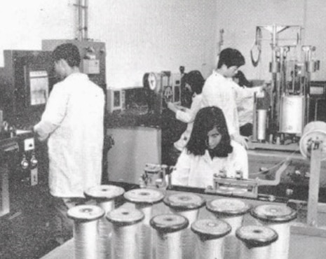 Black-and-white photo of researchers in lab coats examining textile production and research equipment at Hyosung’s R&DB Labs